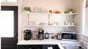 Una cocina con estantes blancos, una cafetera, un tostador, un microondas y un lavabo.