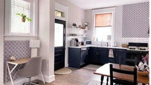Una cocina moderna con armarios oscuros, encimera blanca y zona de comedor con mesa y sillas.