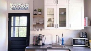 A modern kitchen with white cabinets, a black door, a coffee maker, a kettle, a microwave, and a dishwasher.