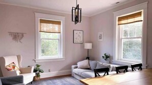 A modern living room with a dining table, two sofas, a chandelier, and large windows with blinds.
