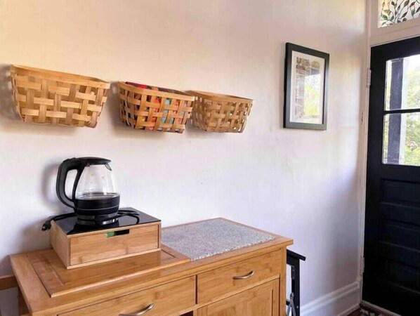 A wooden cabinet with a kettle and a framed picture on the wall.