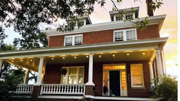 A two-story brick house with a porch, steps, and string lights.