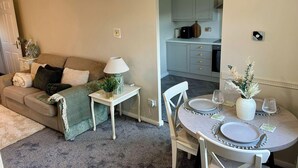 A cozy living room with a sofa, a small table with a lamp, and a dining area with a round table set for two. - Peak District - 2 Beds - Sleeps 4 - Pet Friendly (Chesterfield)