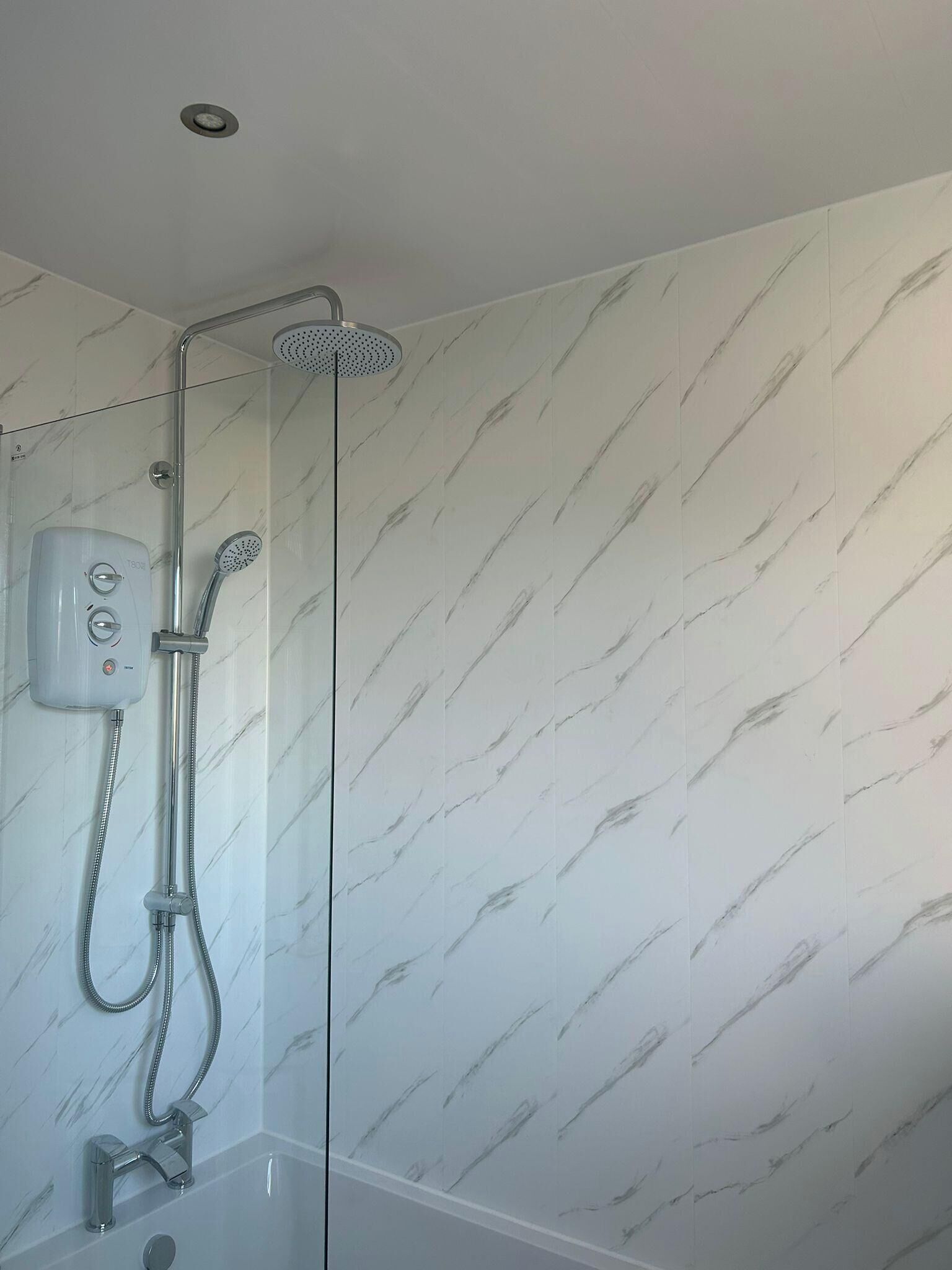 A shower with a handheld showerhead and a wall-mounted control panel.