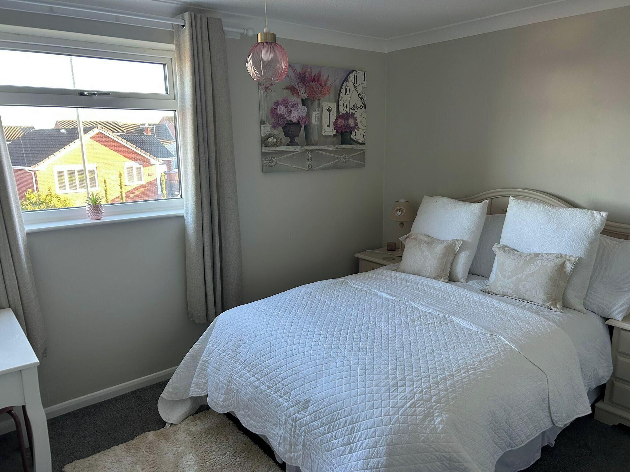 A bedroom with a large bed, a bedside table, a lamp, and a window with curtains.