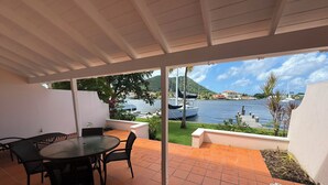 Eine überdachte Terrasse mit Tisch und Stühlen, Blick auf ein Gewässer und Boote.