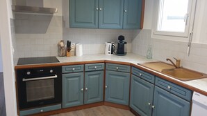 Een keuken met blauwgroene kastjes, een fornuis, een vaatwasser en een spoelbak.