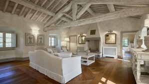 A spacious living room with a high wooden ceiling, a white sofa, a coffee table, and a fireplace. - Villa Mandorla by My Villa Collection (Barberino Tavarnelle)