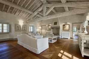 A spacious living room with a high wooden ceiling, a white sofa, a coffee table, and a fireplace.