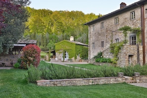 Un edificio de piedra con jardín, un patio cubierto y una pequeña casa con techo verde.