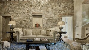 A room with a stone wall, a chandelier, a sofa, two lamps, and a coffee table with books. - Villa Mandorla by My Villa Collection (Barberino Tavarnelle)