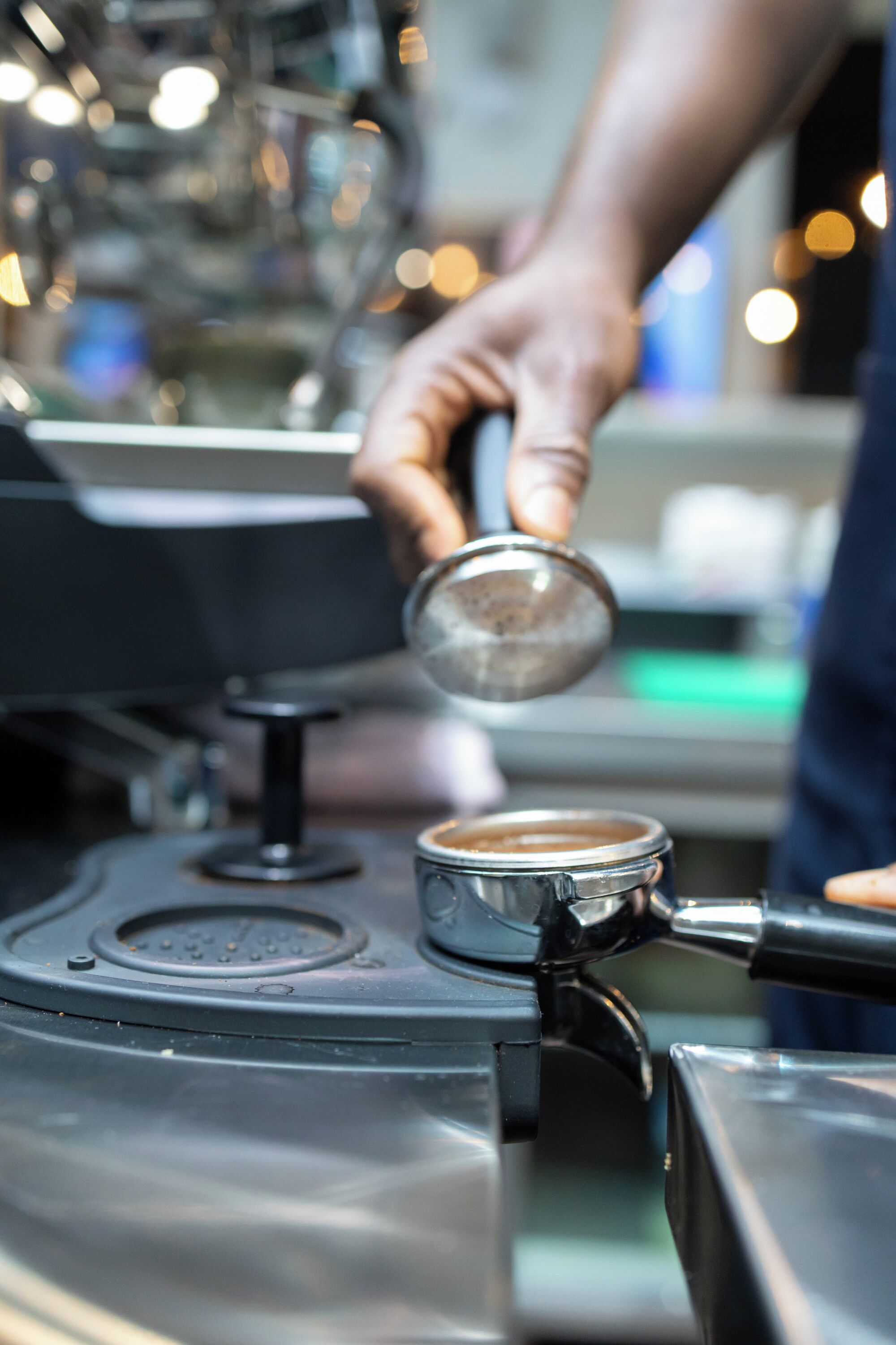 A close-up of a hand holding a coffee grinder above a coffee machine, with a cup of coffee below.