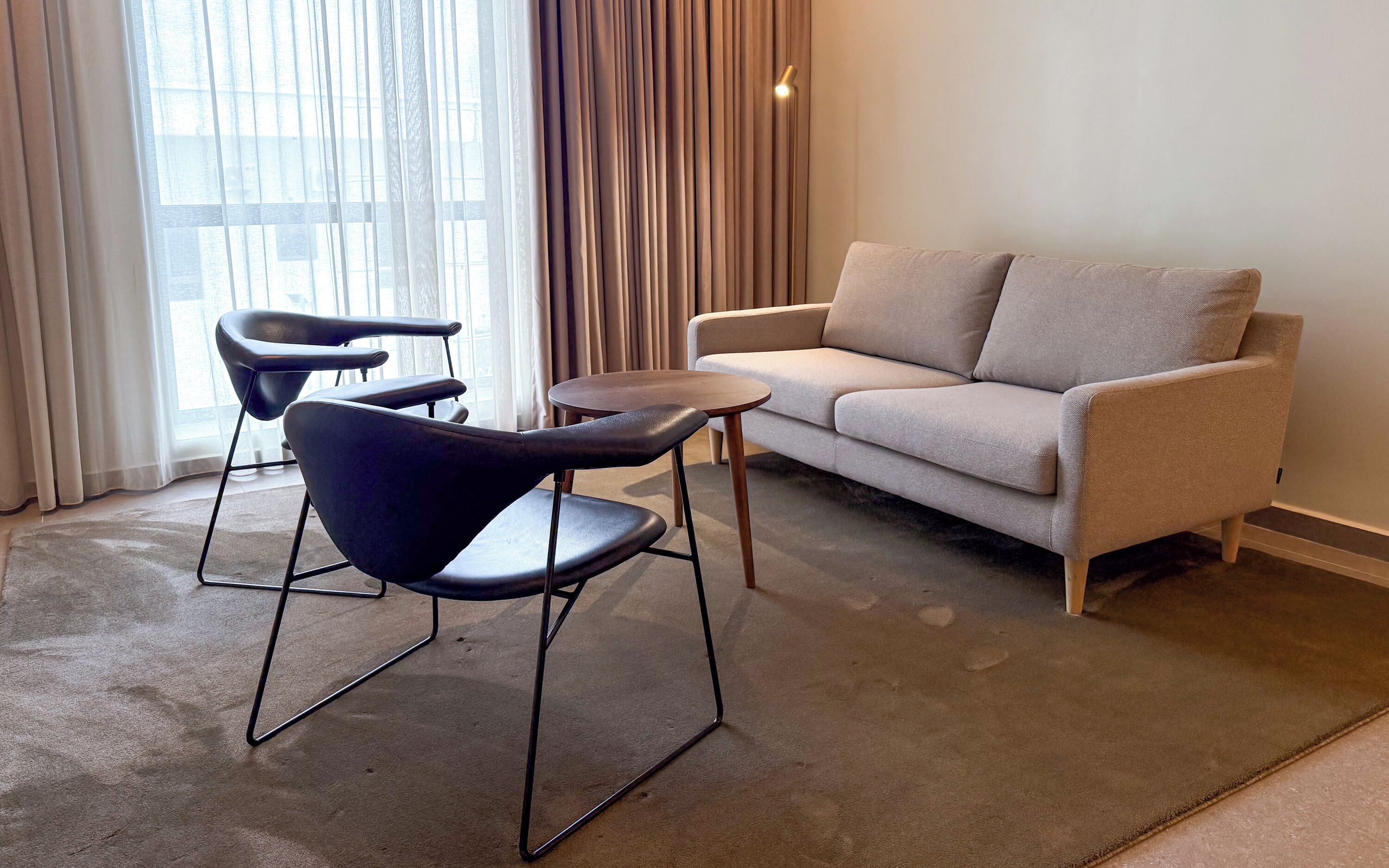 A modern living room with a sofa, two chairs, a small table, and a lamp.