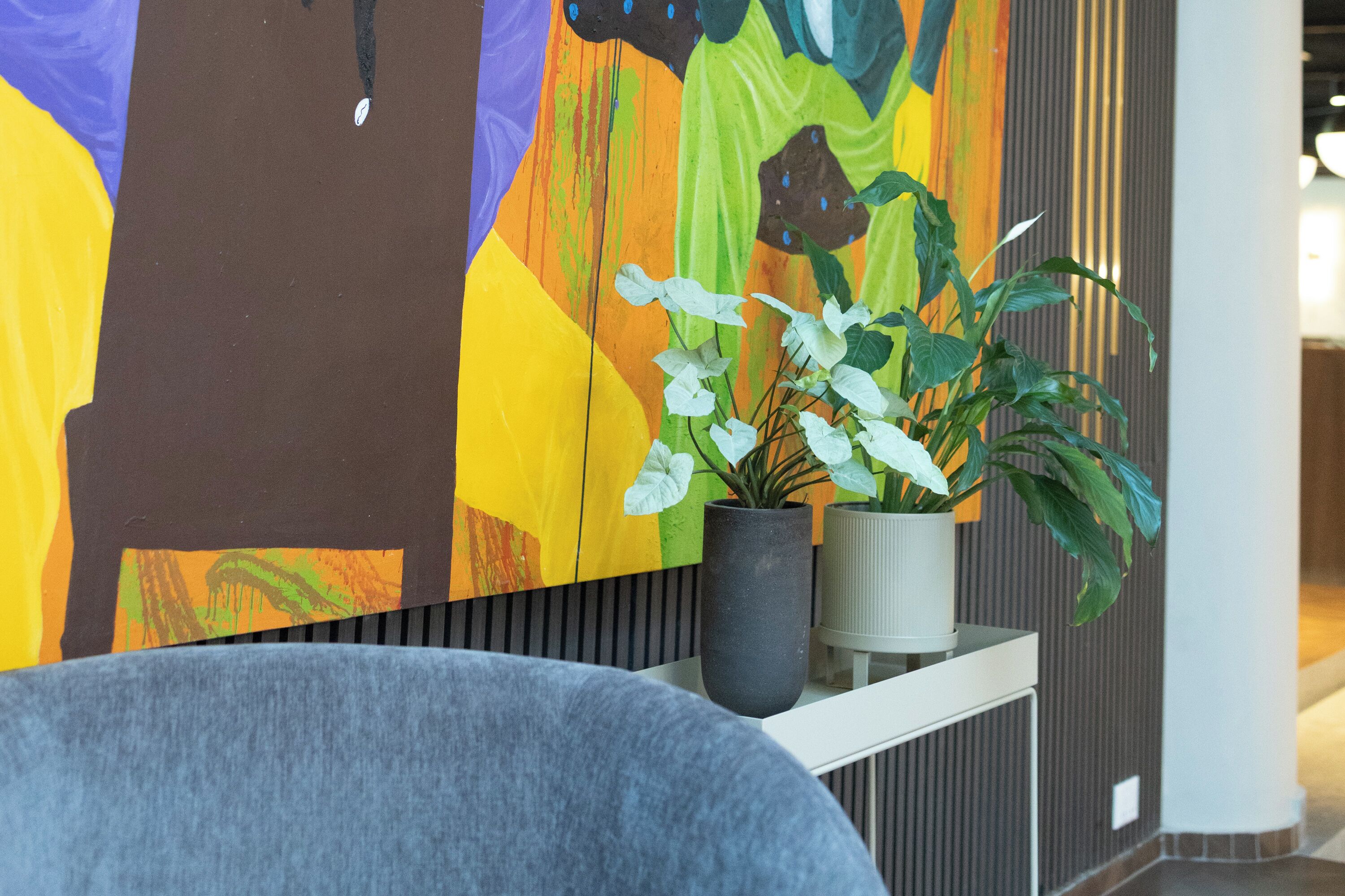 Un interior moderno con un cuadro abstracto vibrante, una planta en maceta y un sillón tapizado en gris.