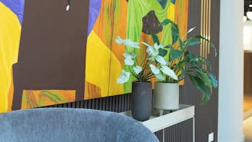 Un interior moderno con un cuadro abstracto vibrante, una planta en maceta y un sillón tapizado en gris.