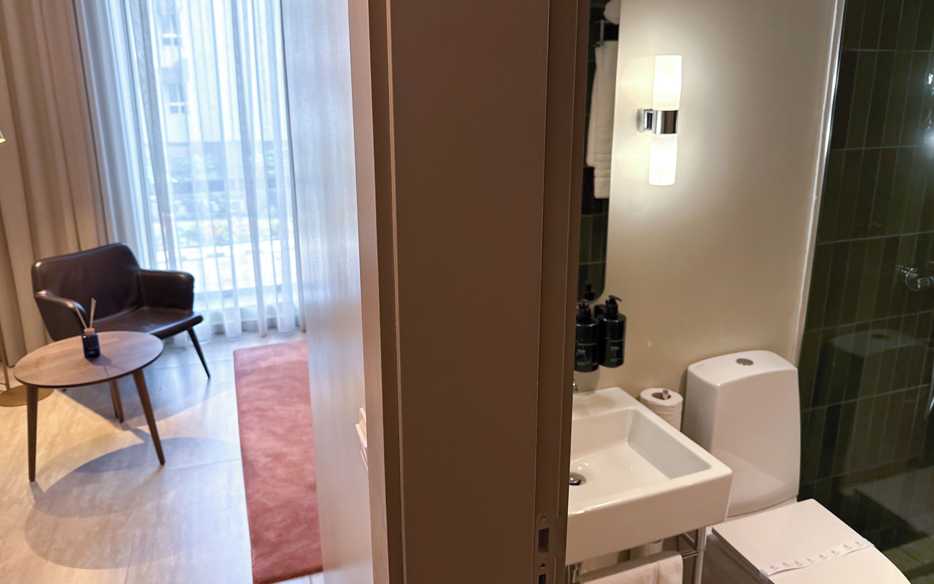 A hotel room with a seating area, a bathroom with a sink and toilet, and a glass shower enclosure.