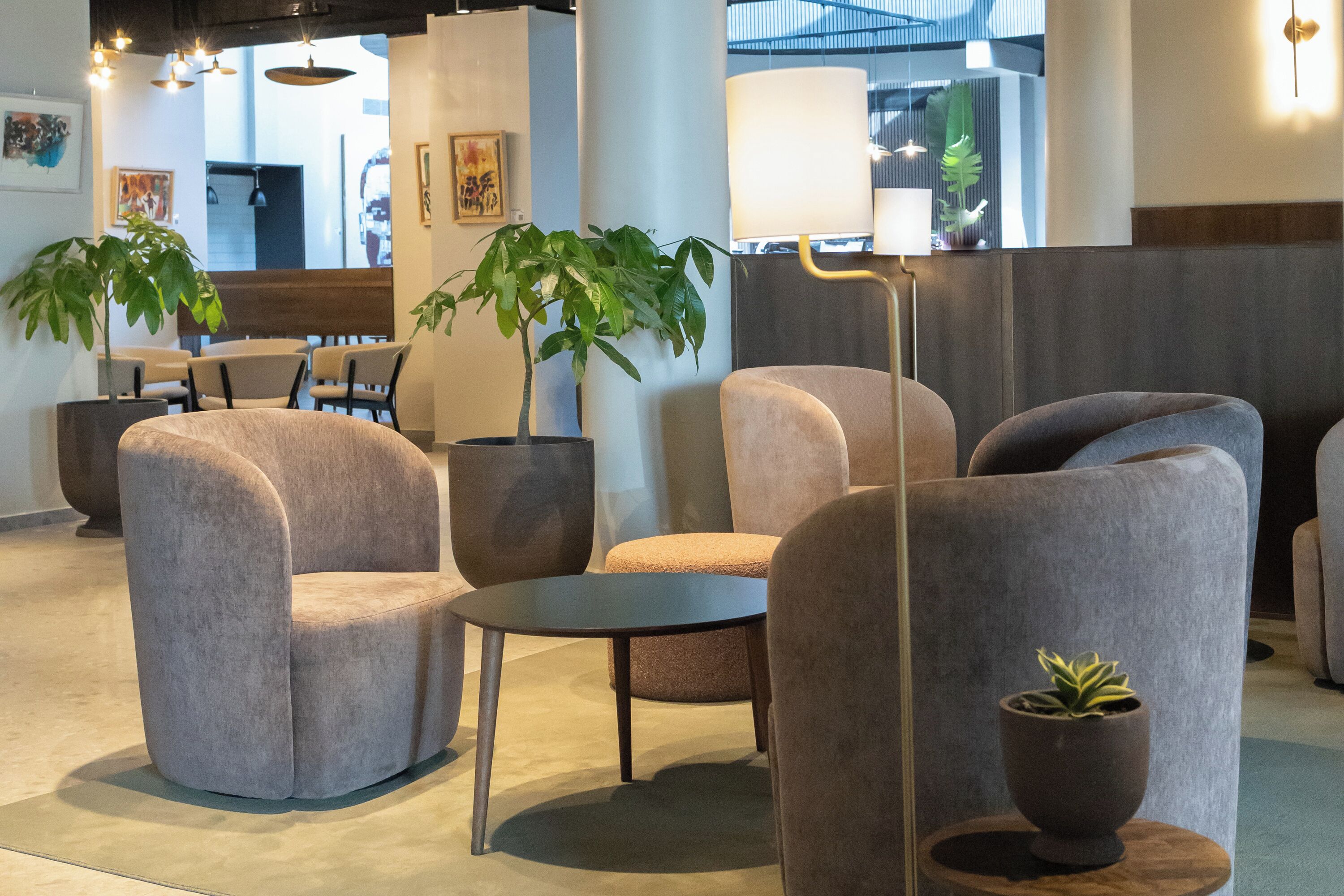 A modern lounge area with plush armchairs, a small round table, and potted plants.