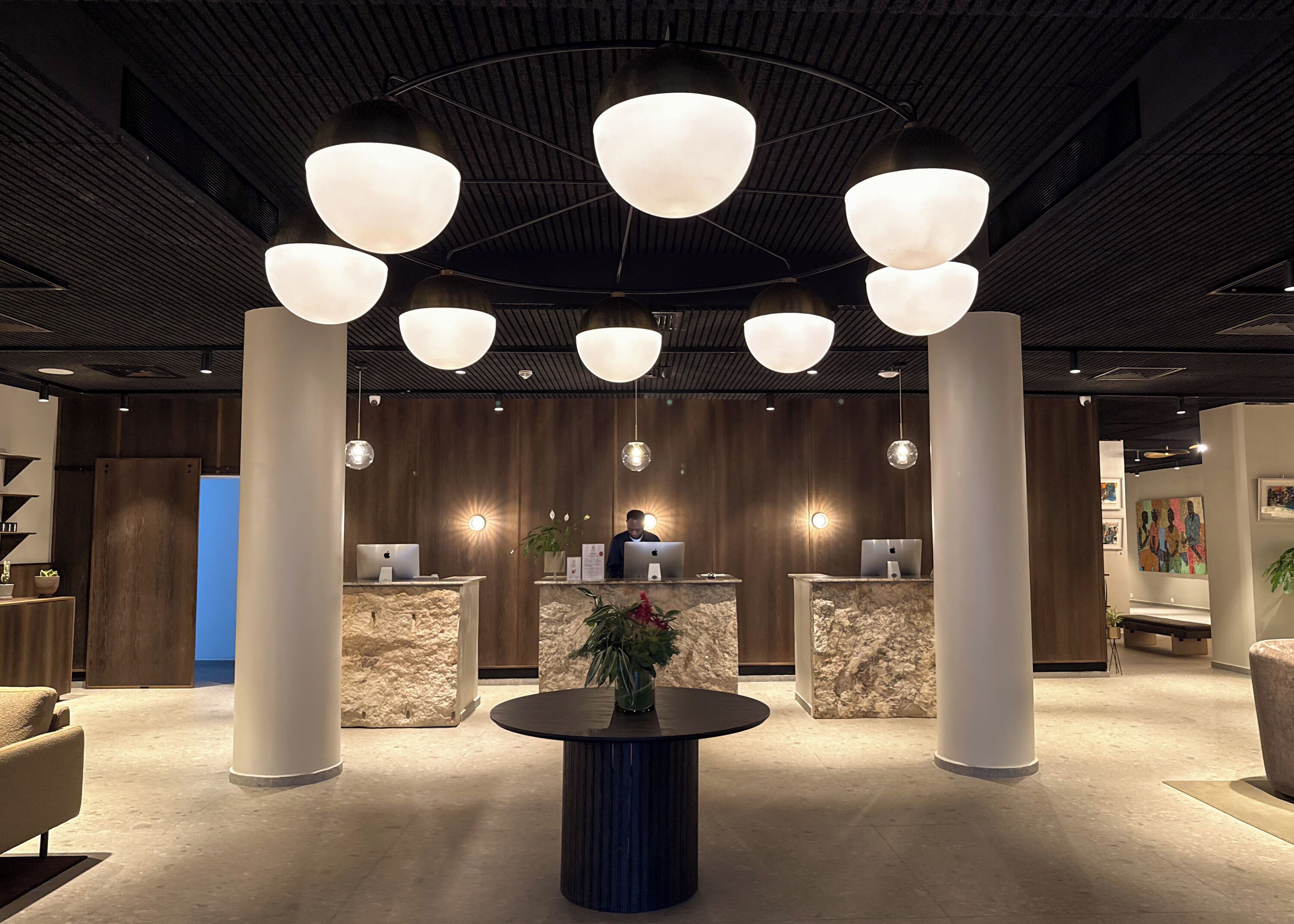 A modern reception area with a central desk, multiple light fixtures, and a round table with a plant.