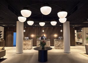 A modern reception area with a central desk, multiple light fixtures, and a round table with a plant. - The Nordic Abuja (Abuja)