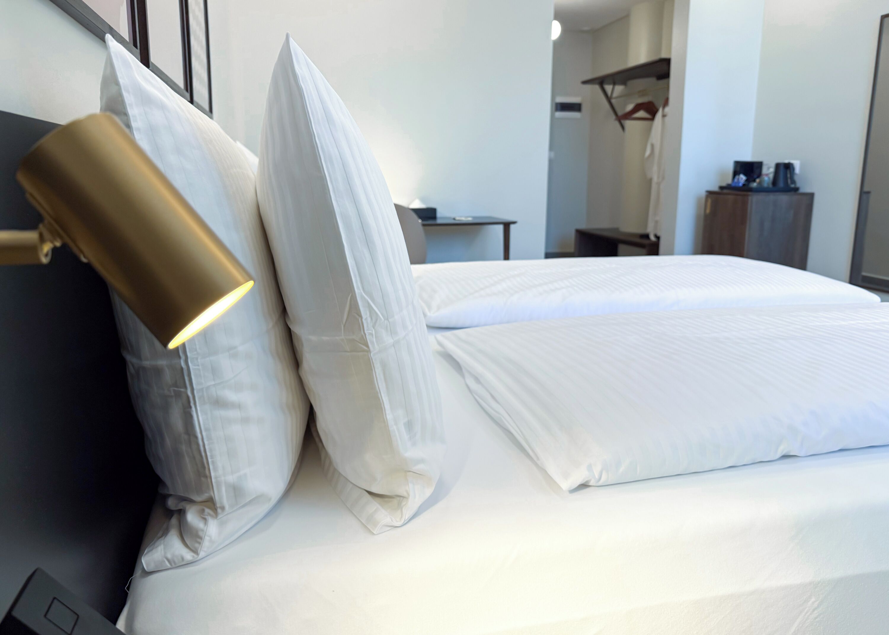 A neatly made bed with white linens and a gold lamp on the left side.