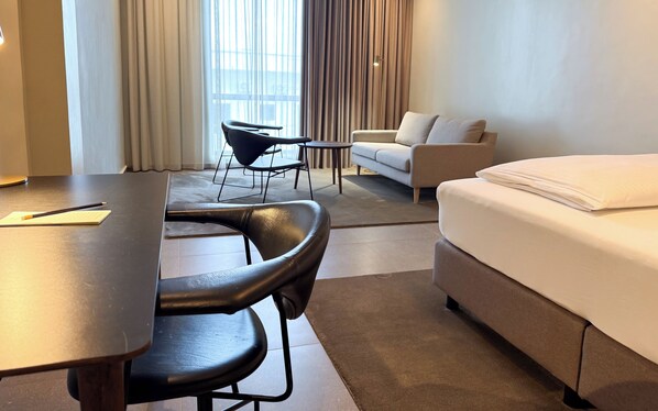 A hotel room with a bed, a desk, a chair, a sofa, and a window with curtains. - The Nordic Abuja (Abuja)