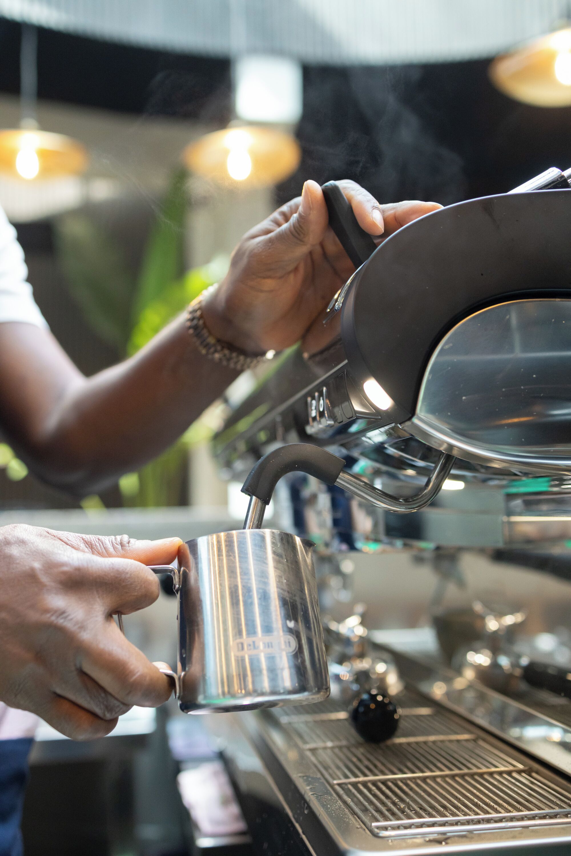 Iemand giet koffie in een metalen beker met behulp van een koffieapparaat.