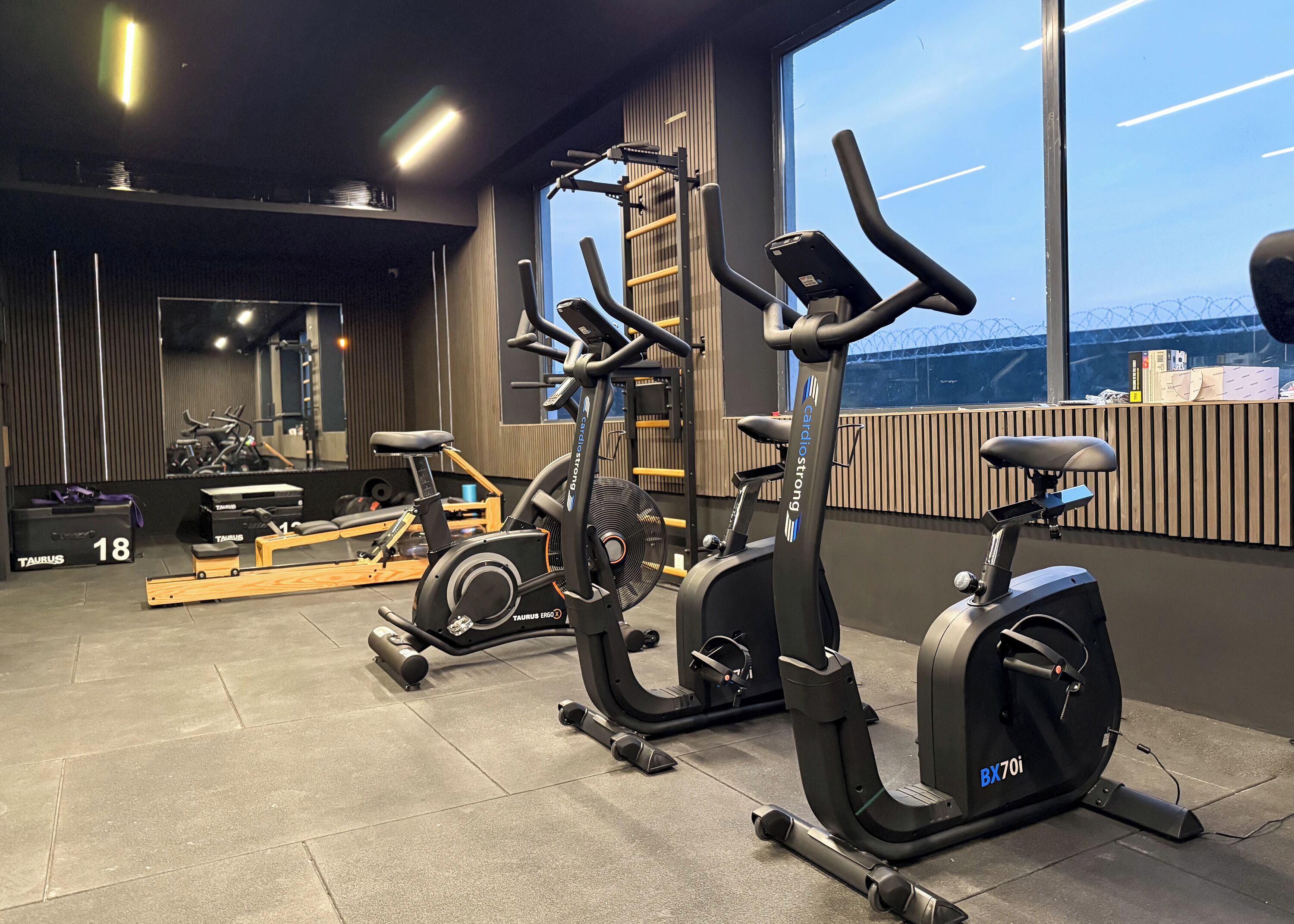 A gym with cardio machines, weightlifting equipment, and a large window with a view of the city.