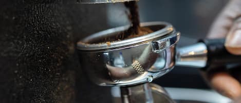 Um close-up de uma máquina de café com acabamento metálico, uma mão ajustando uma alavanca e uma jarra de café embaixo.