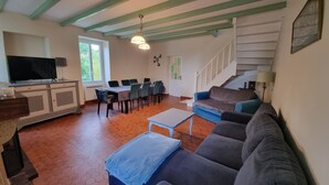 Ett rymligt vardagsrum med en soffa, ett soffbord, en TV, ett matbord med stolar och en trappa.