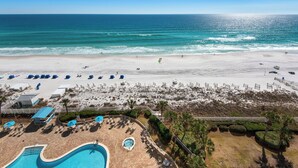 A beach resort with a swimming pool, sun loungers, and a view of the ocean.