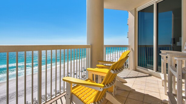 A balcony with yellow chairs overlooking a beach and ocean.