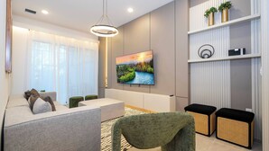 A modern living room with a sofa, a coffee table, a TV mounted on the wall, and a decorative shelf with plants.