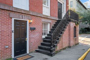 A red brick building with a black front door, a small porch, and a black metal staircase leading to the second floor.