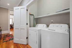 A laundry room with two white front-loading washers and dryers, a green mop, and a white door leading to another room.