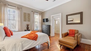 A bedroom with a large bed, a chair, a TV, and a door leading to a bathroom. - No Car Needed+King Bed+Balcony - Abercorn and York (Savannah)