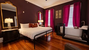 A bedroom with a bed, bedside tables, a mirror, a window with curtains, and a radiator.