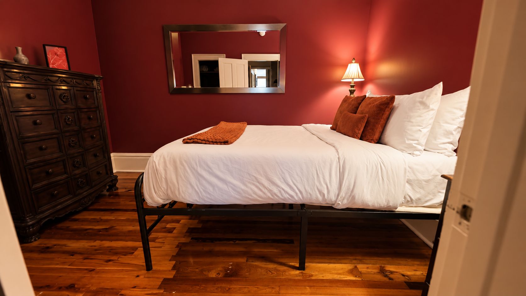 A bedroom with a bed, dresser, mirror, and lamp.