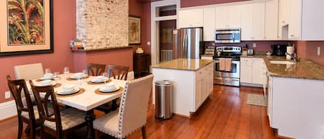 A modern kitchen with white cabinetry, stainless steel appliances, and a dining area with wooden chairs and a marble table.