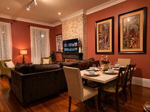 Una sala de estar con chimenea, un comedor con mesa dispuesta para cuatro personas y un televisor montado en la pared.
