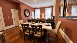 A dining area with a table set for four, surrounded by chairs, in a room with wooden flooring and a red wall. - No Car Needed+King Bed+Balcony - Abercorn and York (Savannah)