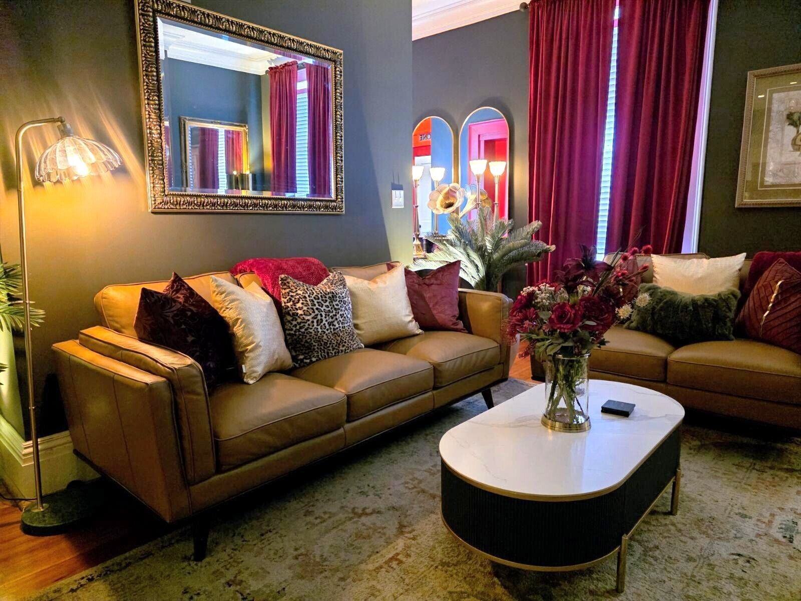A living room with a brown leather sofa, a white coffee table, and a mirror with a decorative frame.