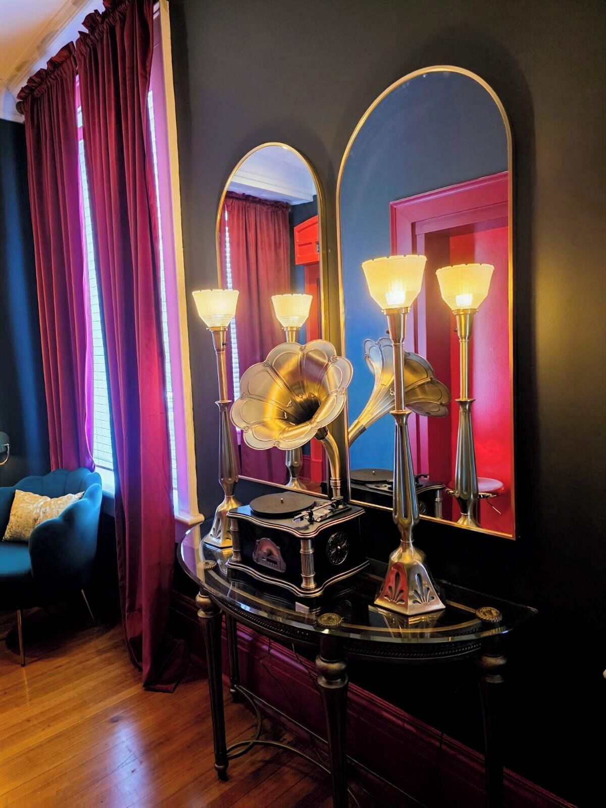 A room with a vintage gramophone, two wall-mounted mirrors, and a blue armchair.