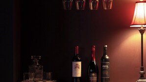 Eine Bar mit drei Weinflaschen, Gläsern und einer Lampe.