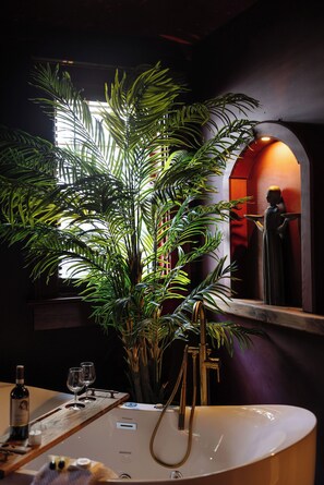 A bathroom with a large potted plant, a mirror, a sink, and a statue.