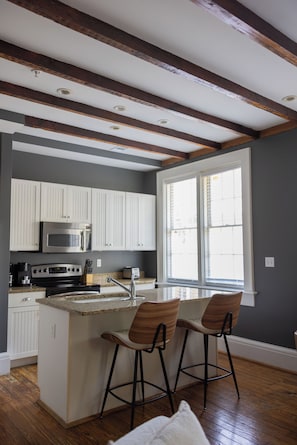 A kitchen with a central island, white cabinets, stainless steel appliances, and a window with blinds. - Jacuzzi Tub! Walk to River Street & King Bed (Savannah)