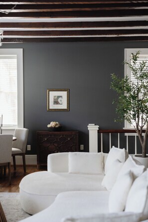 A living room with a white sofa, a dark wall, a framed picture, a plant, and a window with blinds. - Jacuzzi Tub! Walk to River Street & King Bed (Savannah)