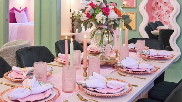 A dining area with a long table set for six, featuring pink and white linens, gold cutlery, and a centerpiece with flowers and candles. - Walk to River Street, Bars, Shopping, and Sleeps 8 (Savannah)