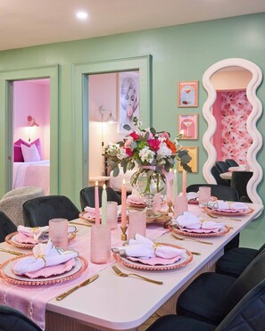 A dining area with a long table set for six, featuring pink and white linens, gold cutlery, and a centerpiece with flowers and candles. - Walk to River Street, Bars, Shopping (Savannah)