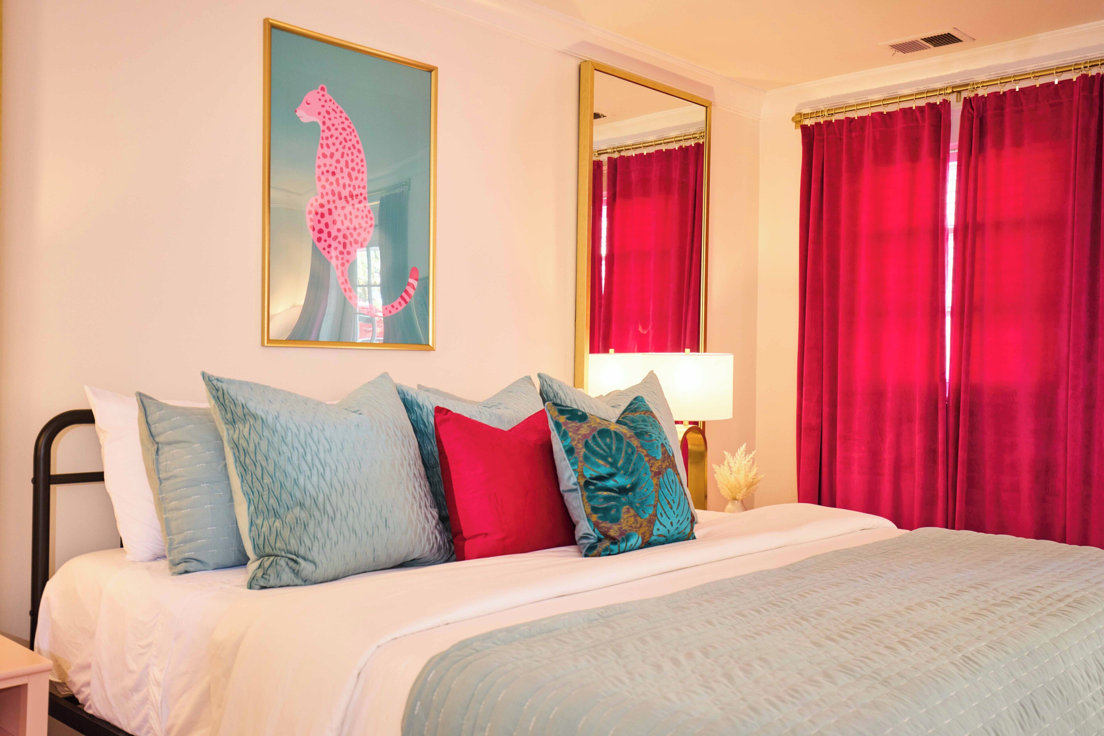 Une chambre d’hôtel avec un lit, des oreillers, un miroir et des rideaux rouges.