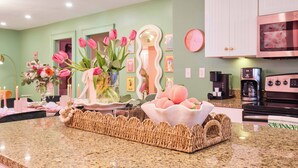A kitchen with a granite countertop, a wicker basket, a bowl of fruit, and a wall-mounted clock. - Walk to River Street, Bars, Shopping, and Sleeps 8 (Savannah)